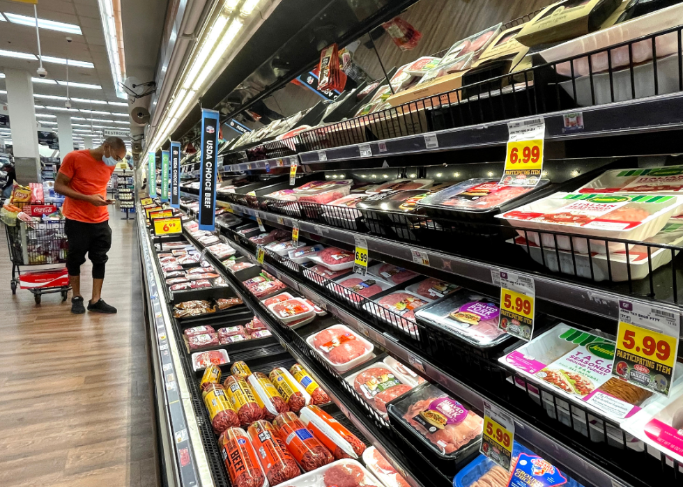 A person shopping in the meat section of a grocery store with high prices