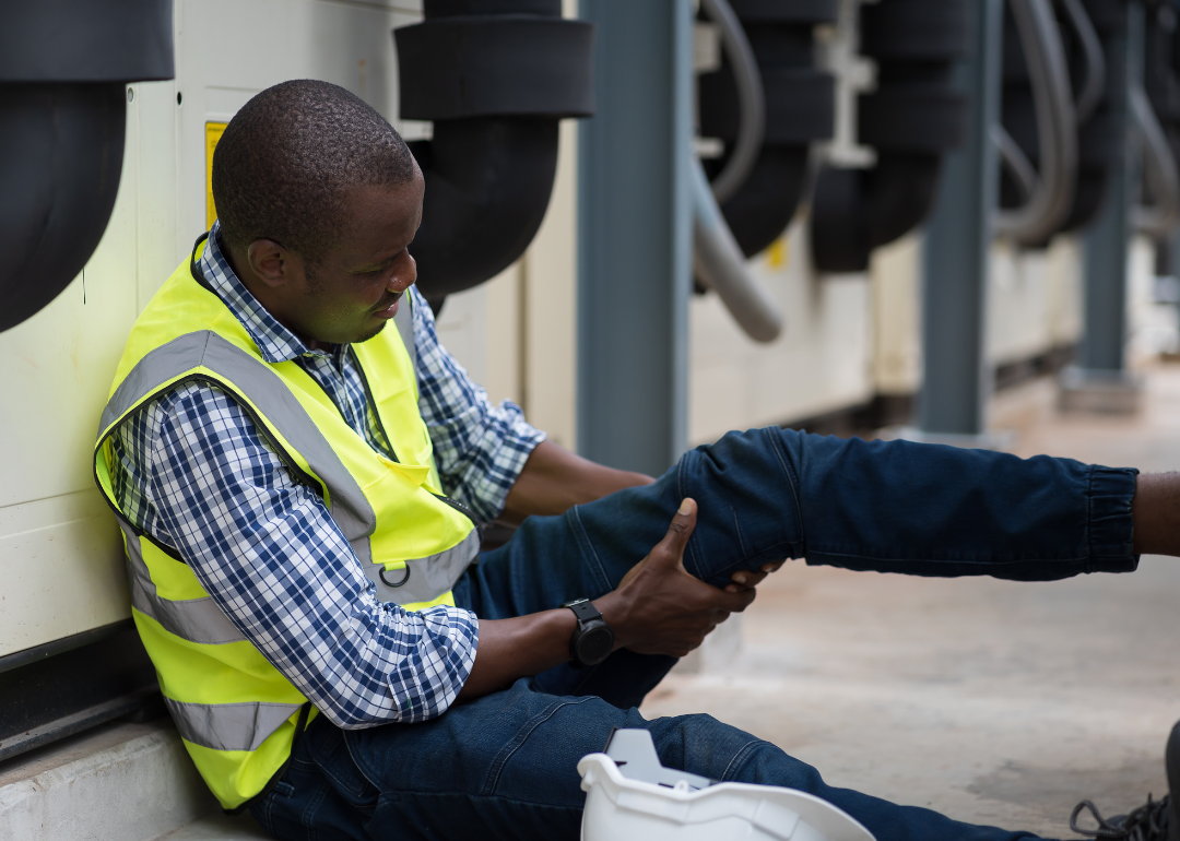 A worker grabbing an injured leg at a construction site.