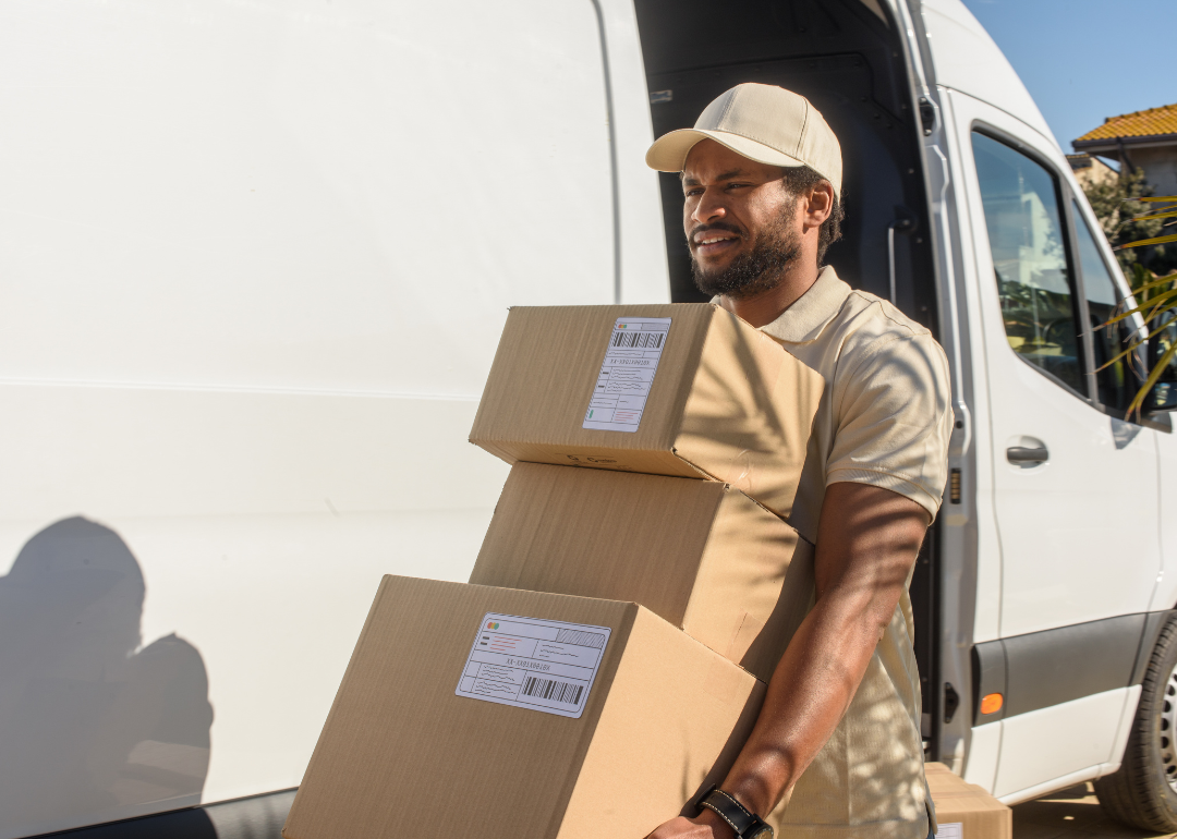 A package courier carrying boxes while squinting in the sunlight.