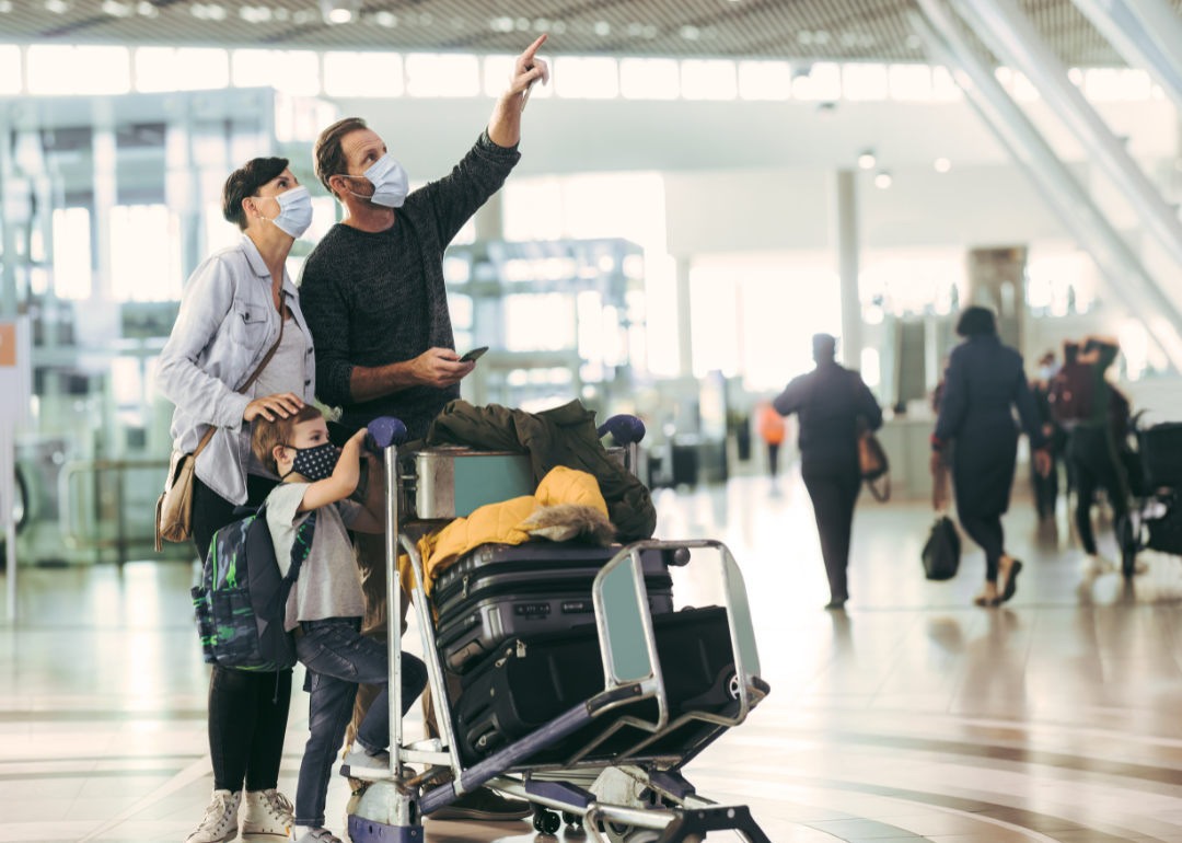 A family with a luggage trolley looking at the arrival/departure board in an airport.
