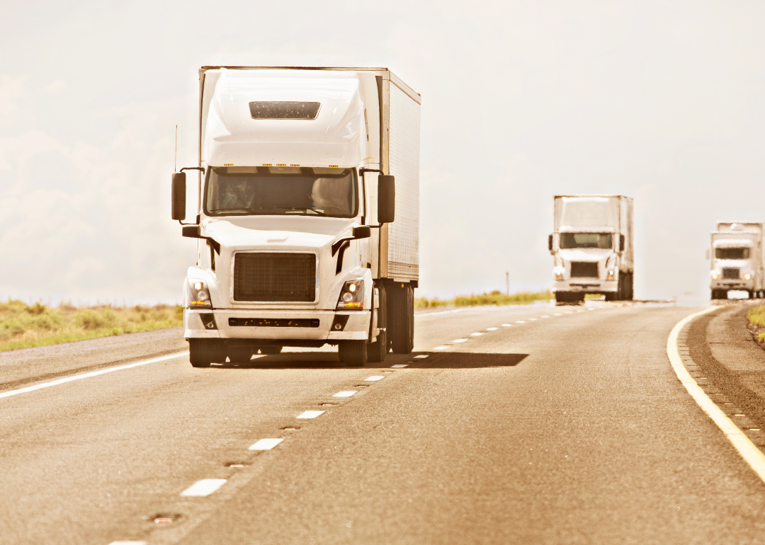 Three identical white trucks driving down a highway.