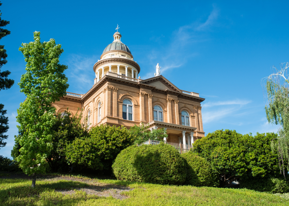 A stately building with a cross atop the domed part of the roof on a sunny day.