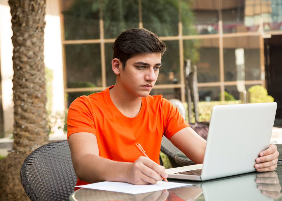 A college student taking notes during an online course