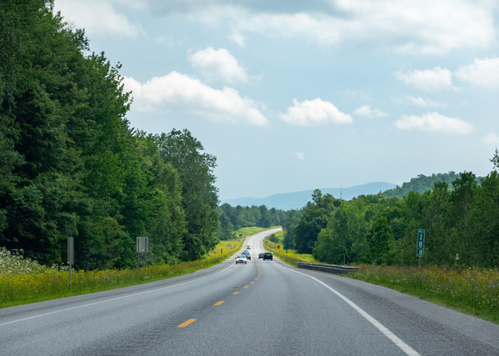 A highway with little traffic surrounded by green woods.