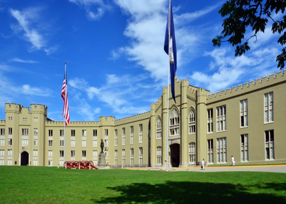 A large stone building with two flags flying and a statue of a person in front of it. 
