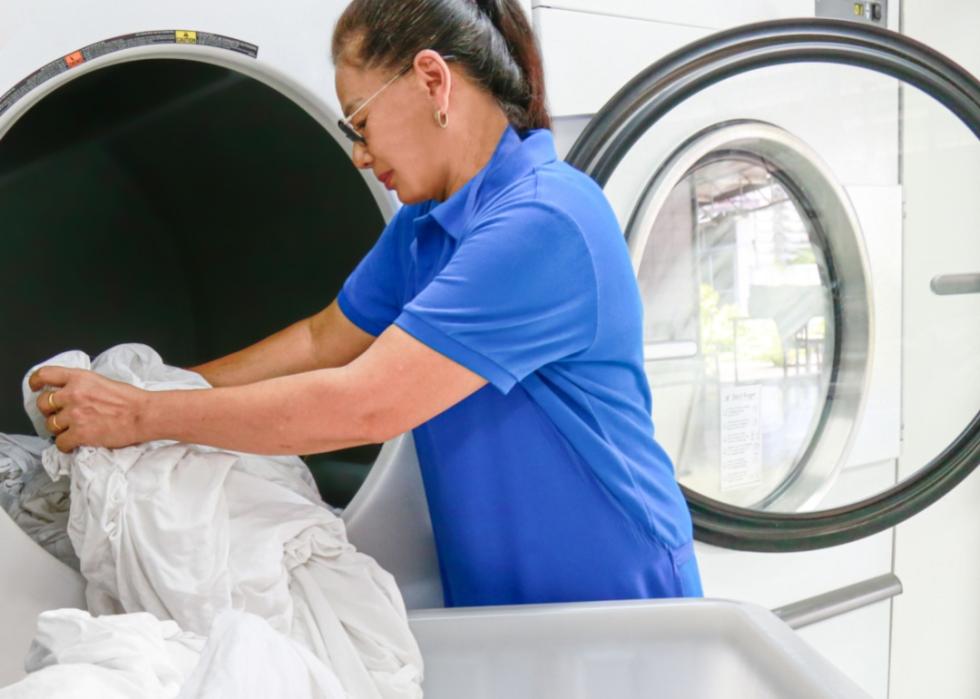 An older woman placing sheets into a dryer.
