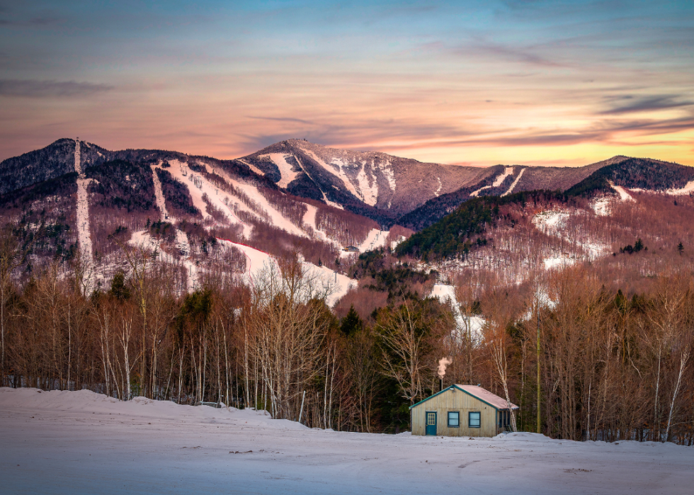 A small, wooden cabin nestled in front of a snow-capped mountain.
