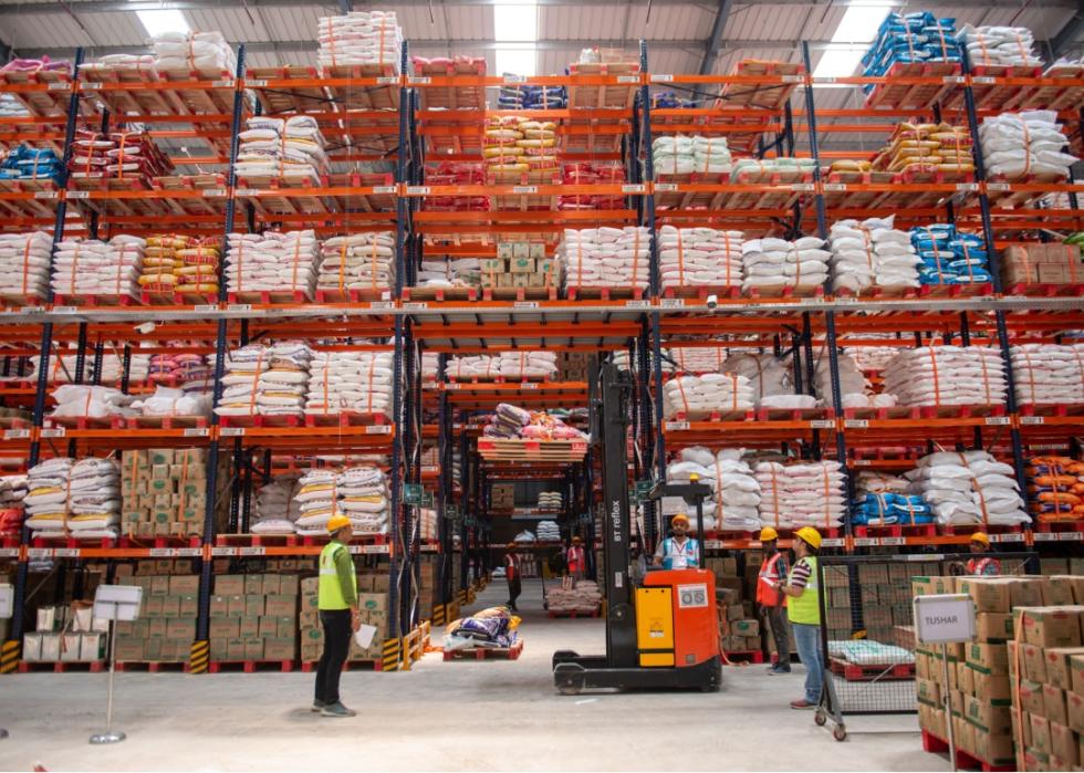 People wearing green vests and helemts are standing in front of tall shelves stacked with various merchandise.