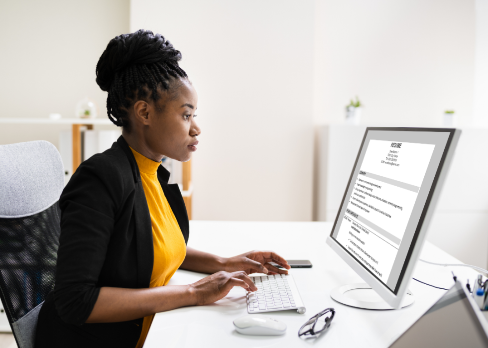 A woman at a desk reading resumes online.
