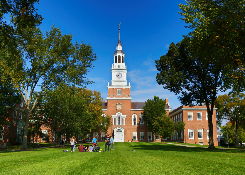 Students on a lawn in front of a red stone building with a clocktower.