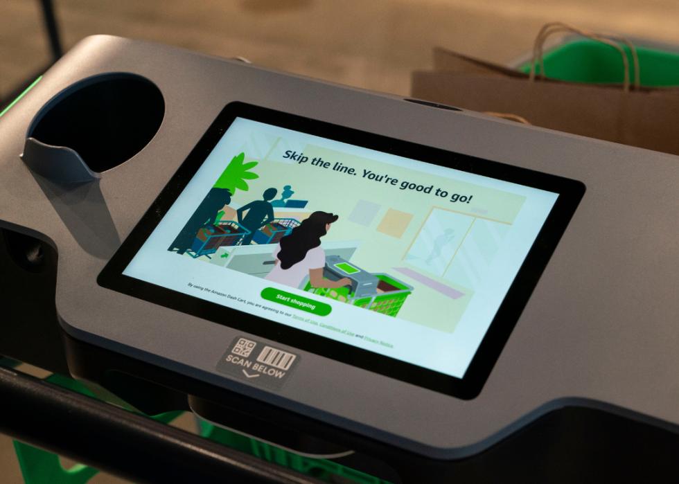 A screen displayed on a cart at an Amazon Fresh. The screen says, "Skip the line. You're good to go" and shows an illustrated person pushing a cart with the technology on it.   