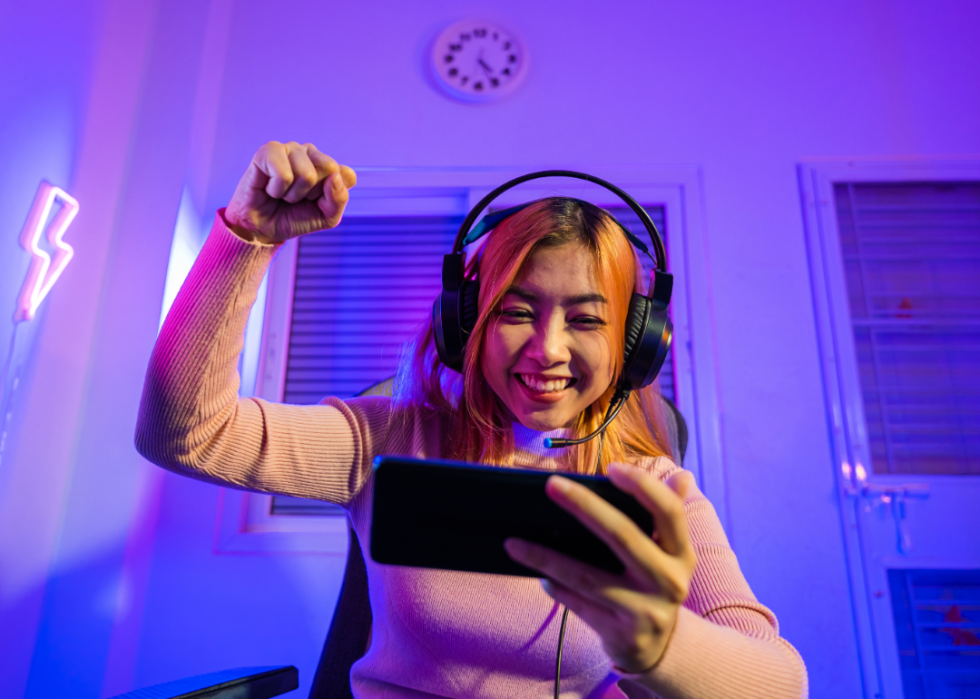 An excited girl sitting in a room with blue light while looking at a phone.