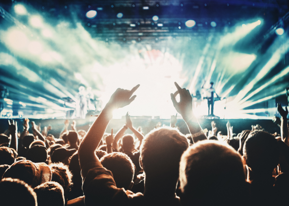 Concert crowd silhouettes with brightly lit stage with a band playing in the background.