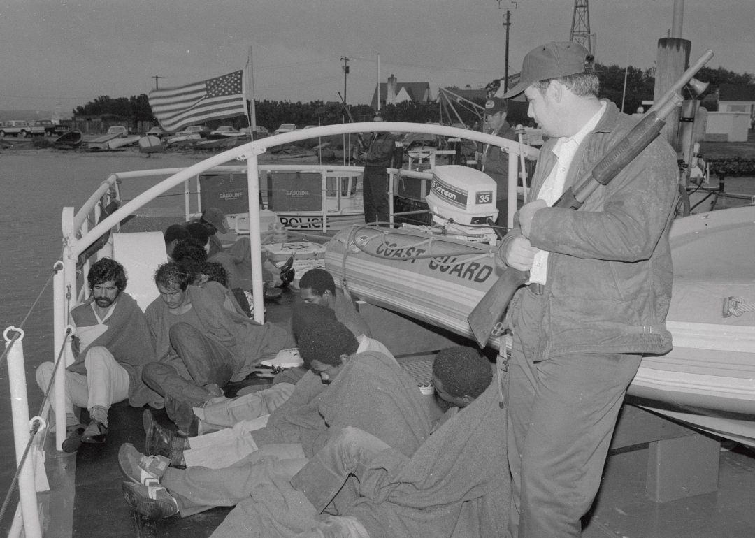 A Coast Guard officer guarding men arrested for drug smuggling on a boat.