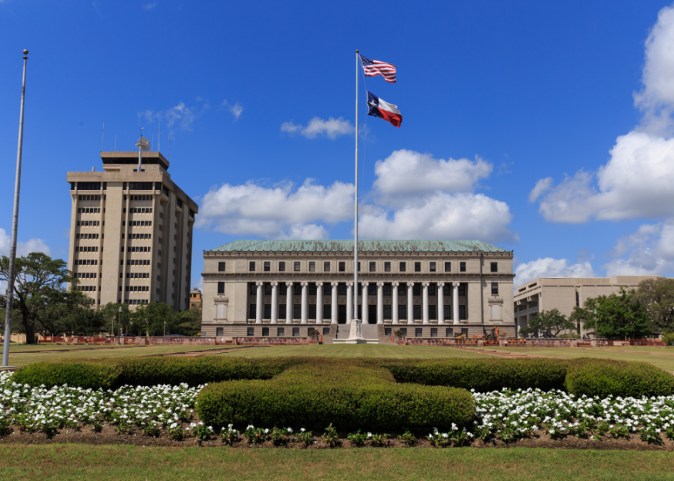 Stately buildings on a college campus with an American and Texas flag flying on a pole.