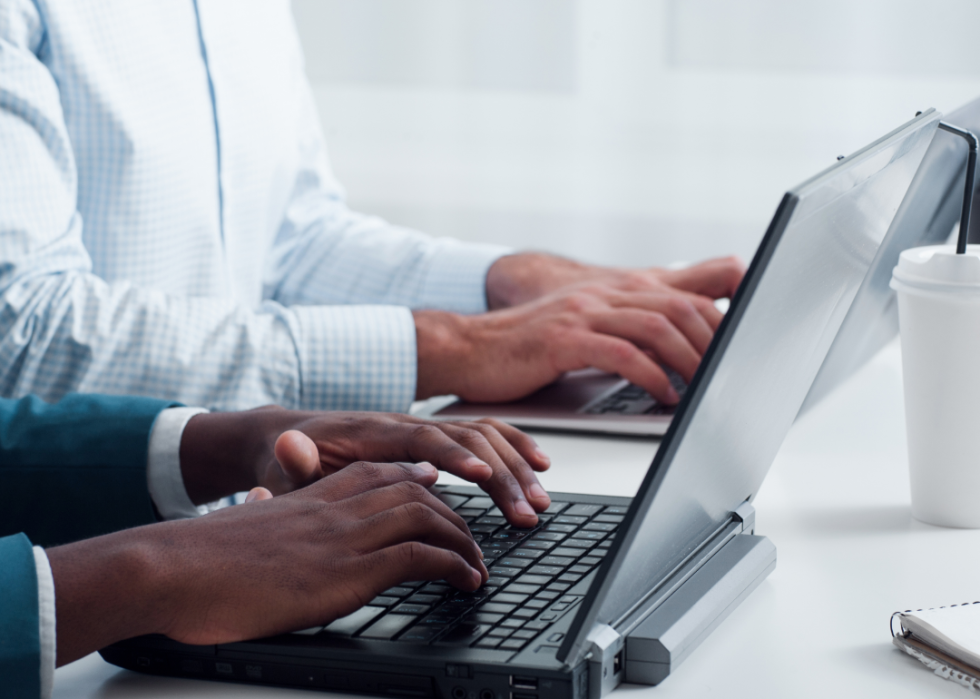 A close up of two pairs of hands typing on laptops.