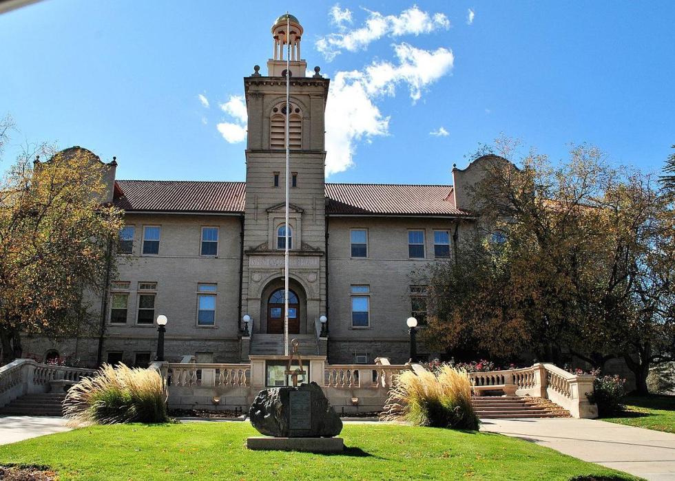 A gray building with a tall tower a large piece of a stone with a placard in front of it.