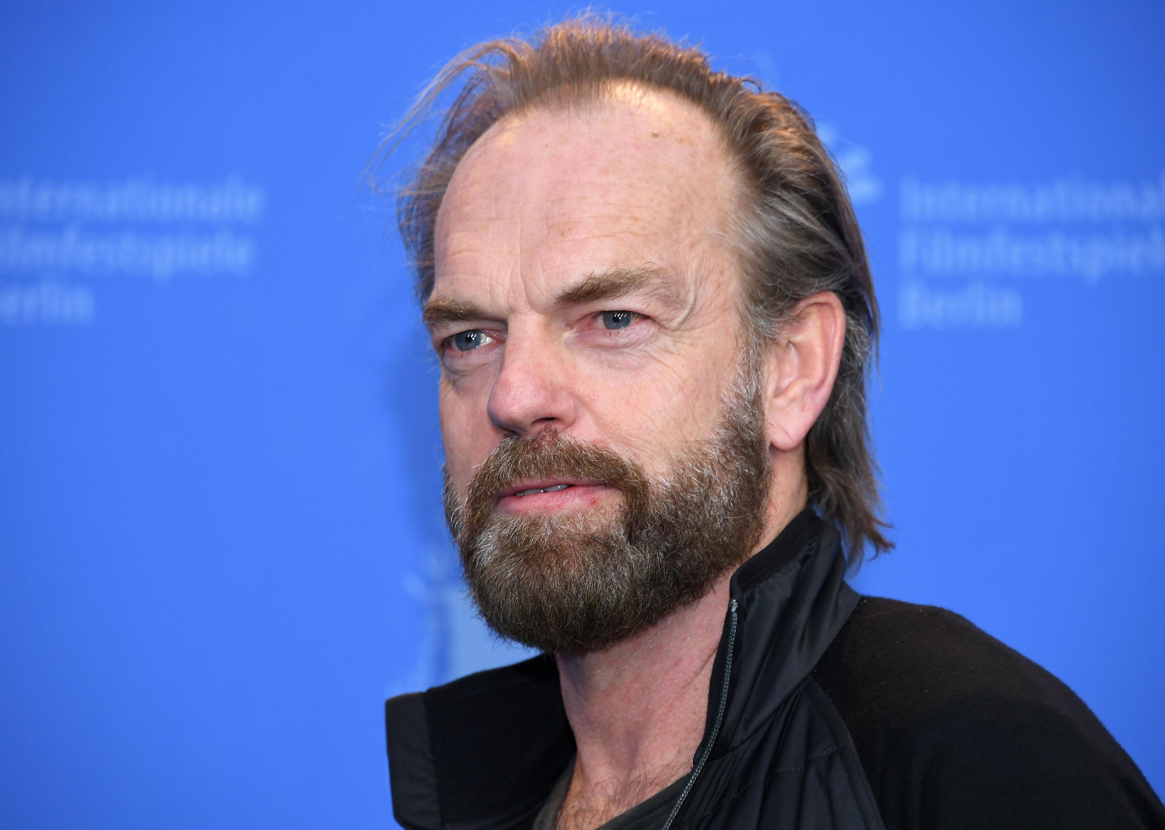 Hugo Weaving in black against a blue background.