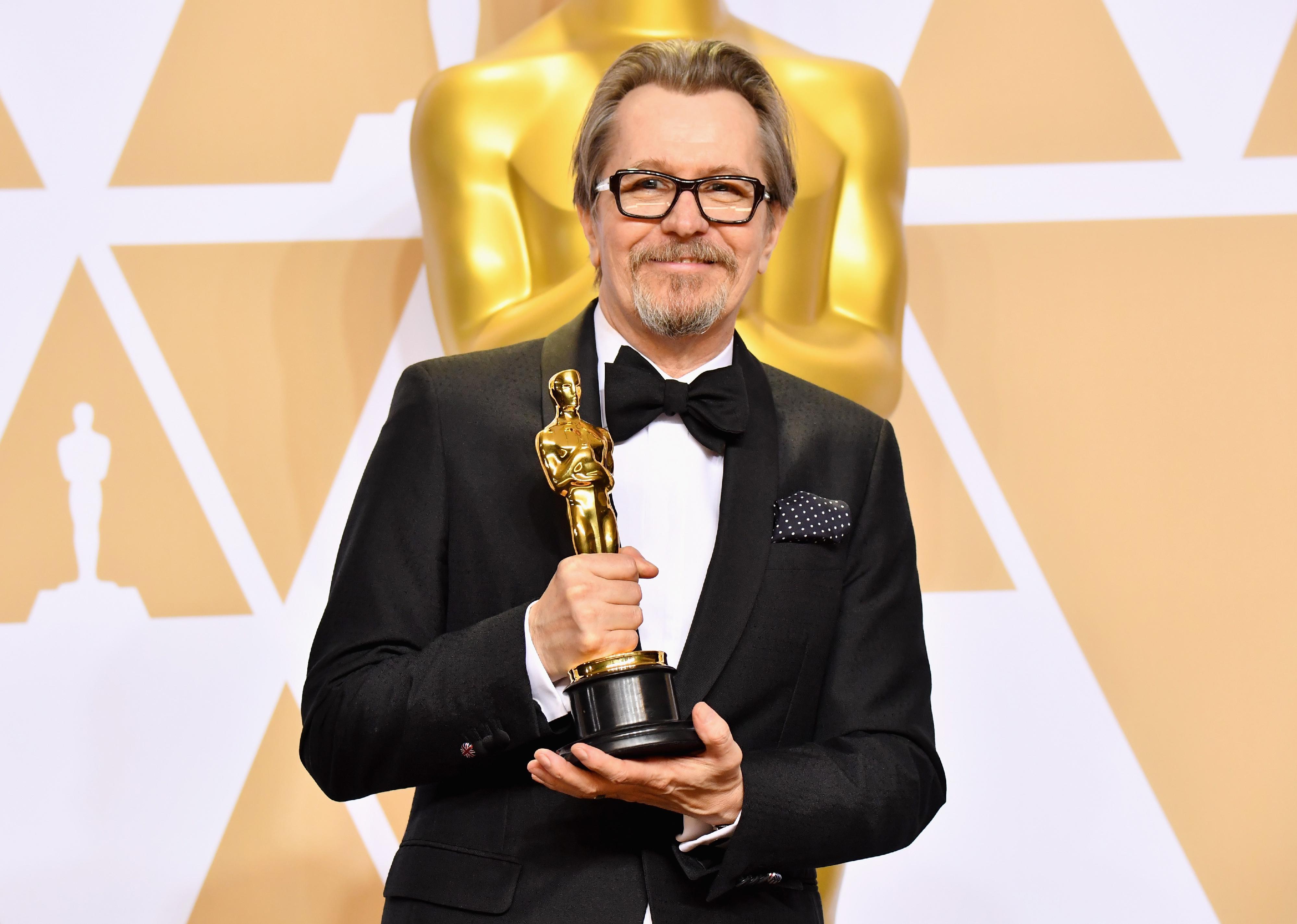 Gary Oldman in a black suit holding an Oscar.