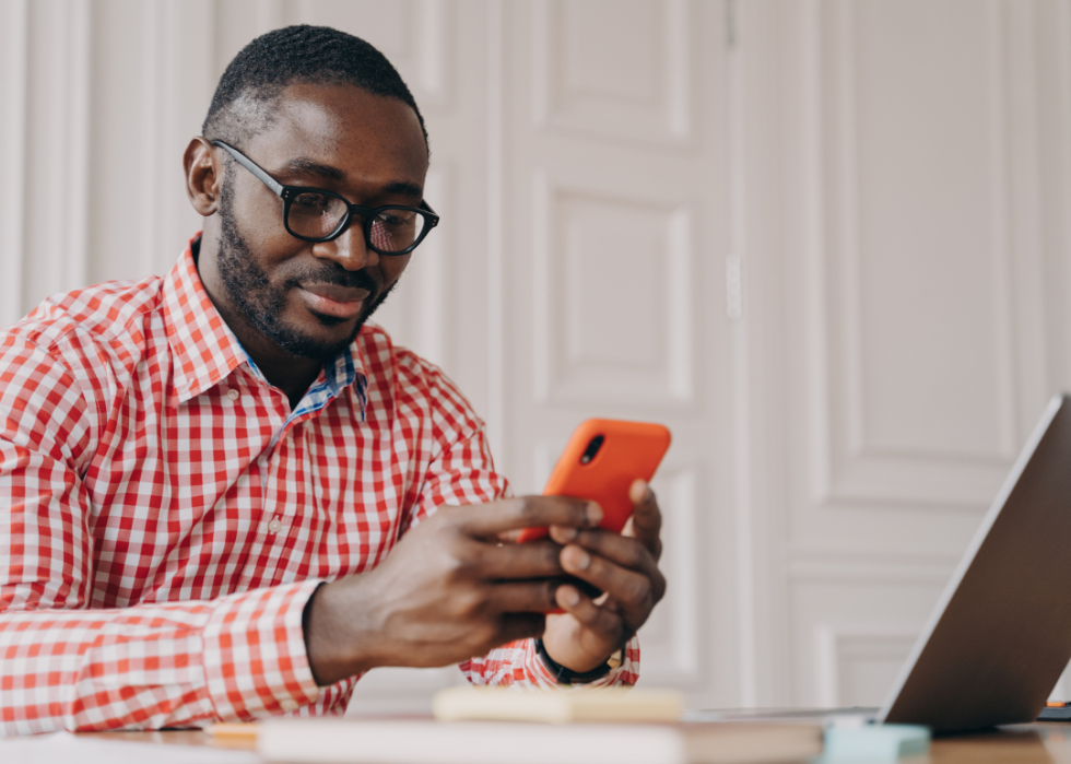 A young man in an orange plaid button down shirt working at a laptop.