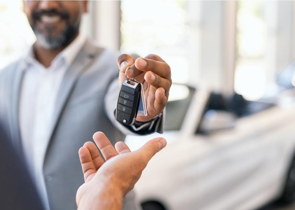 Man with a big smile on his face handing over the keys to a new car.