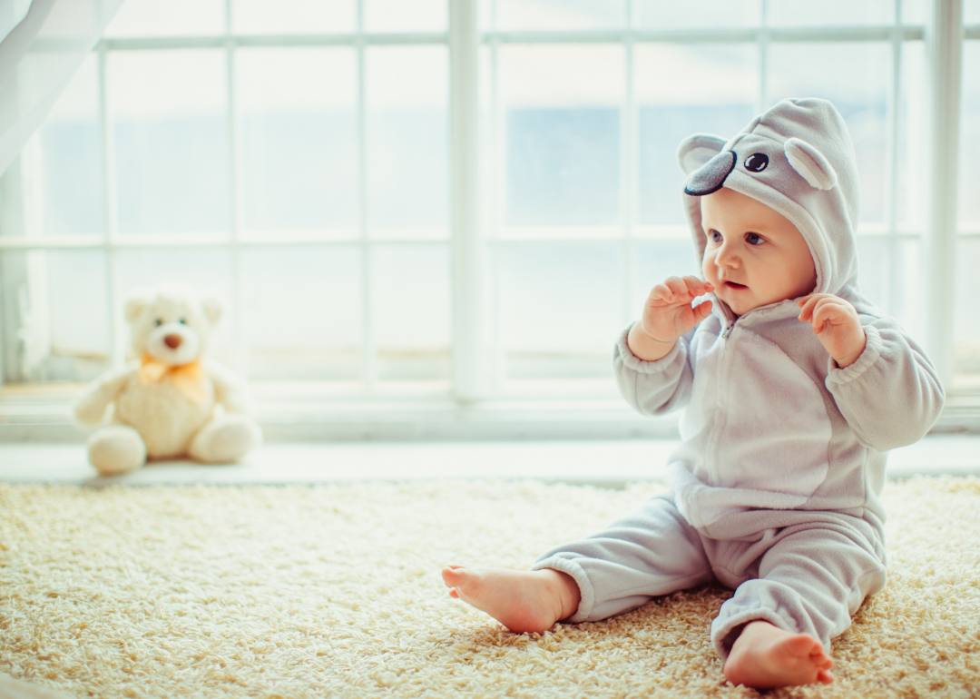 A baby sitting on carpet wearing an elephant outfit.