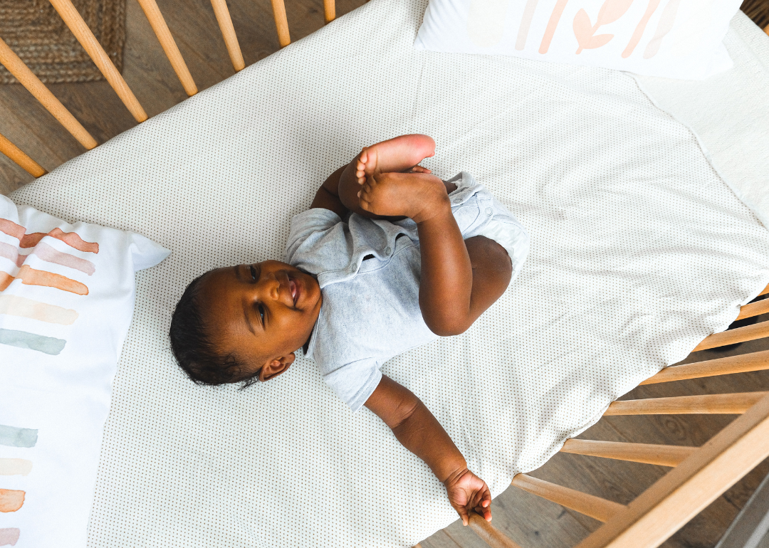 A baby in a wooden crib with pillows.
