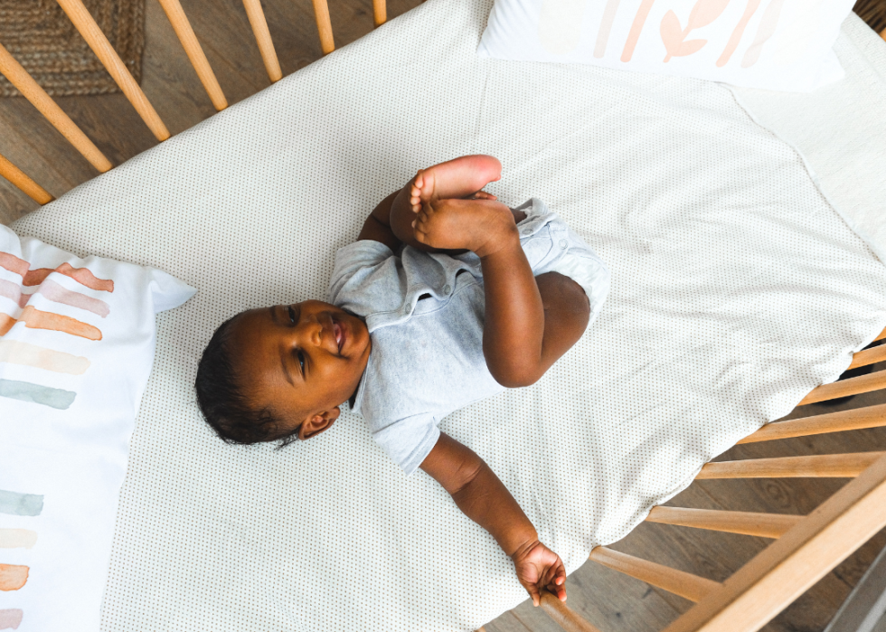 A baby in a wooden crib with pillows.