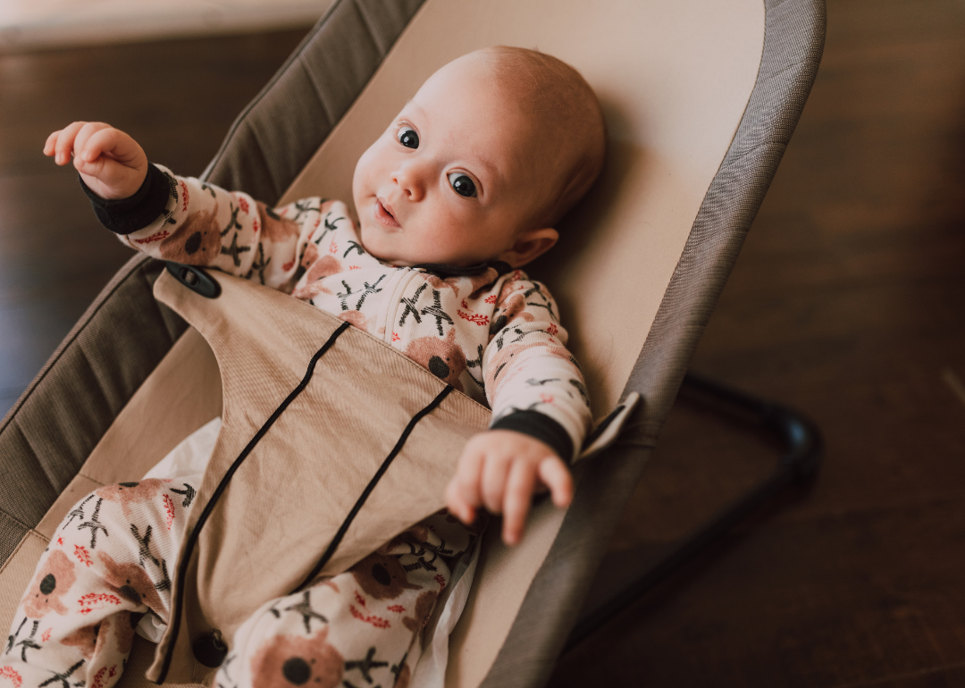 A baby in a colorful outfit in a bouncer.