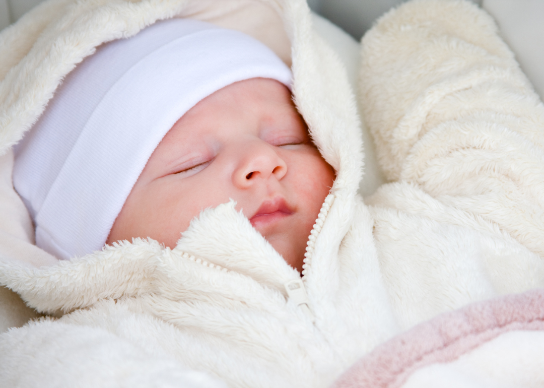 A baby sleeping in a white fluffy zip up suit.