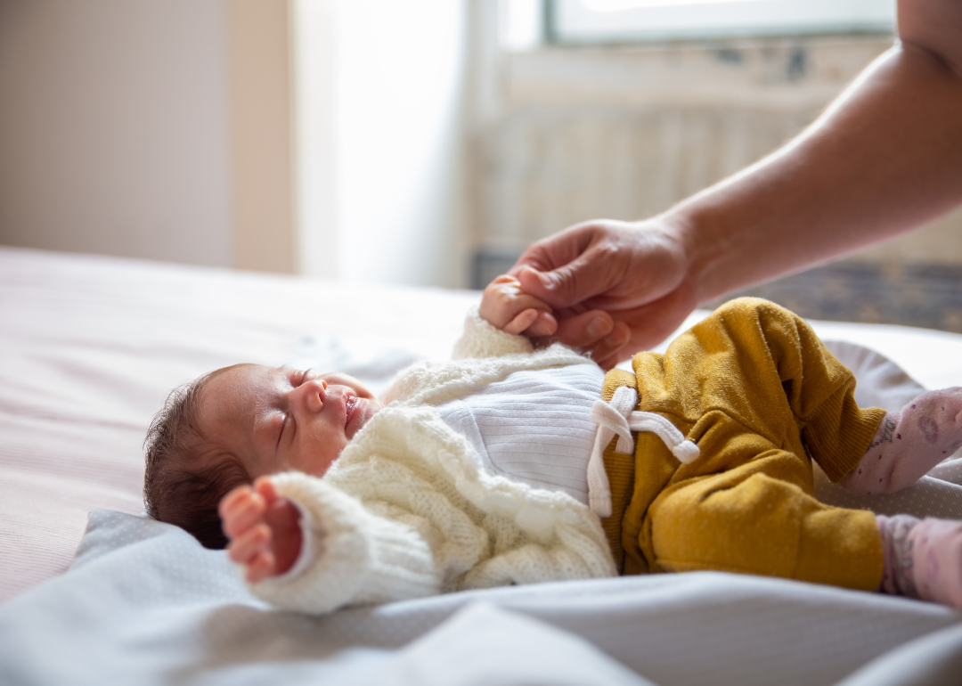 A newborn baby sleeping in mustard colored pants and a white sweater.