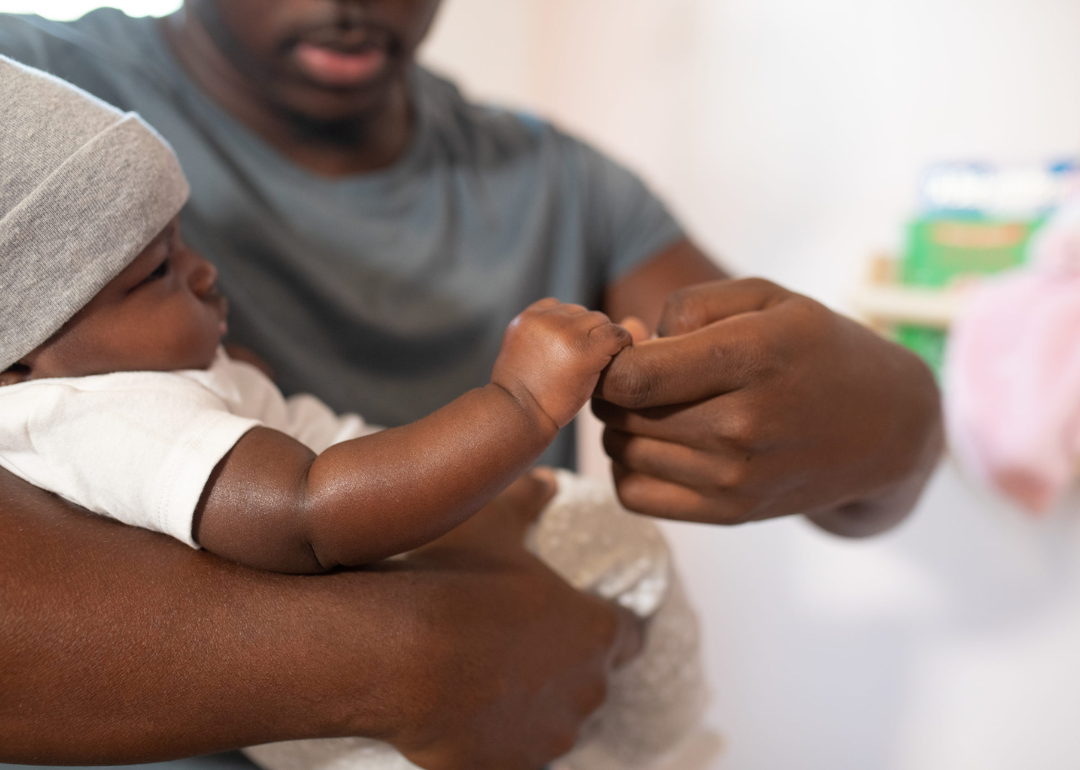 A man carrying a baby in a gray hat and white onesie.