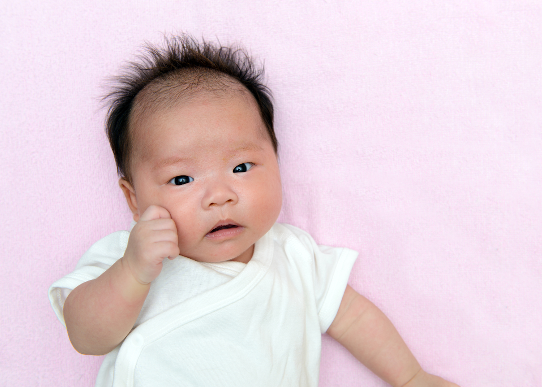 A baby in a white onesie on a pink blanket.