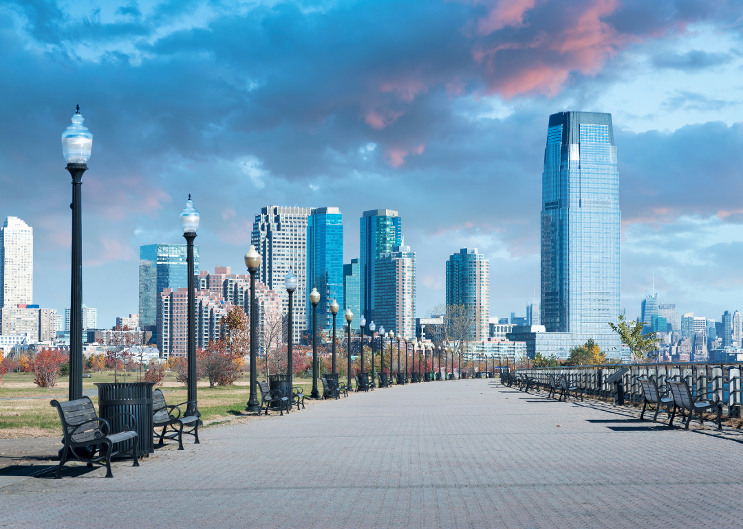 A park lined with benches and lights leading to downtown Jersey City, NJ.