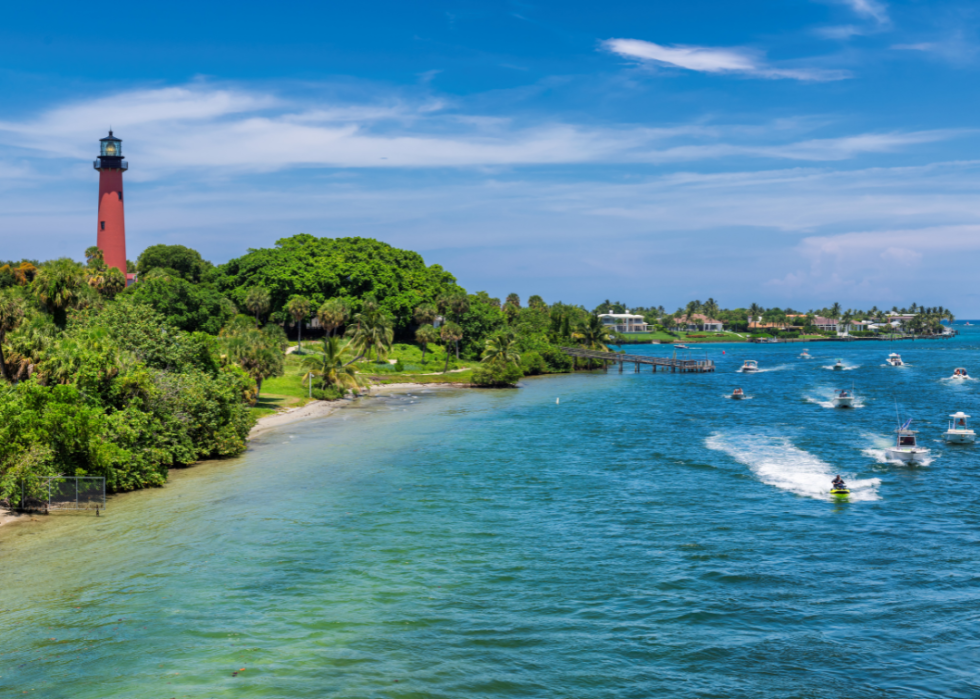 View of lighthouse and inlet facing blue water with speeding boats and jetskis.