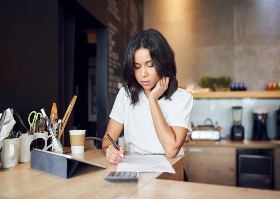A woman filling out paperwork at a table in a kitchen next to a tablet.