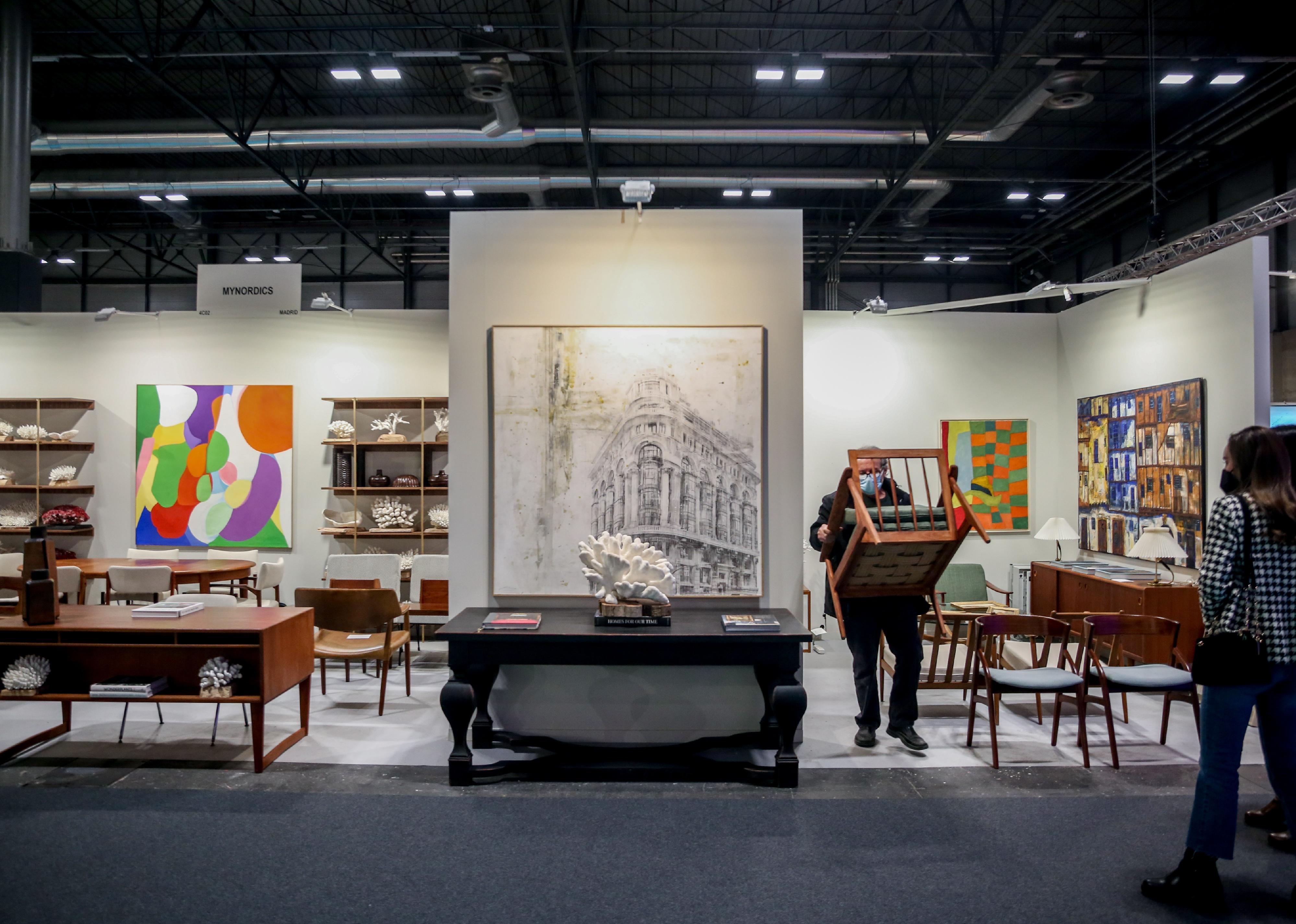 A man carries a chair out of a booth at an antiques and art fair.