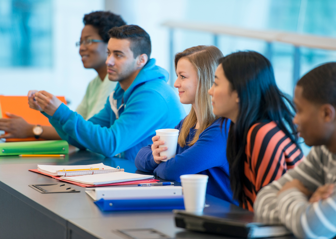 Students sitting in a row with notebooks and paper smiling