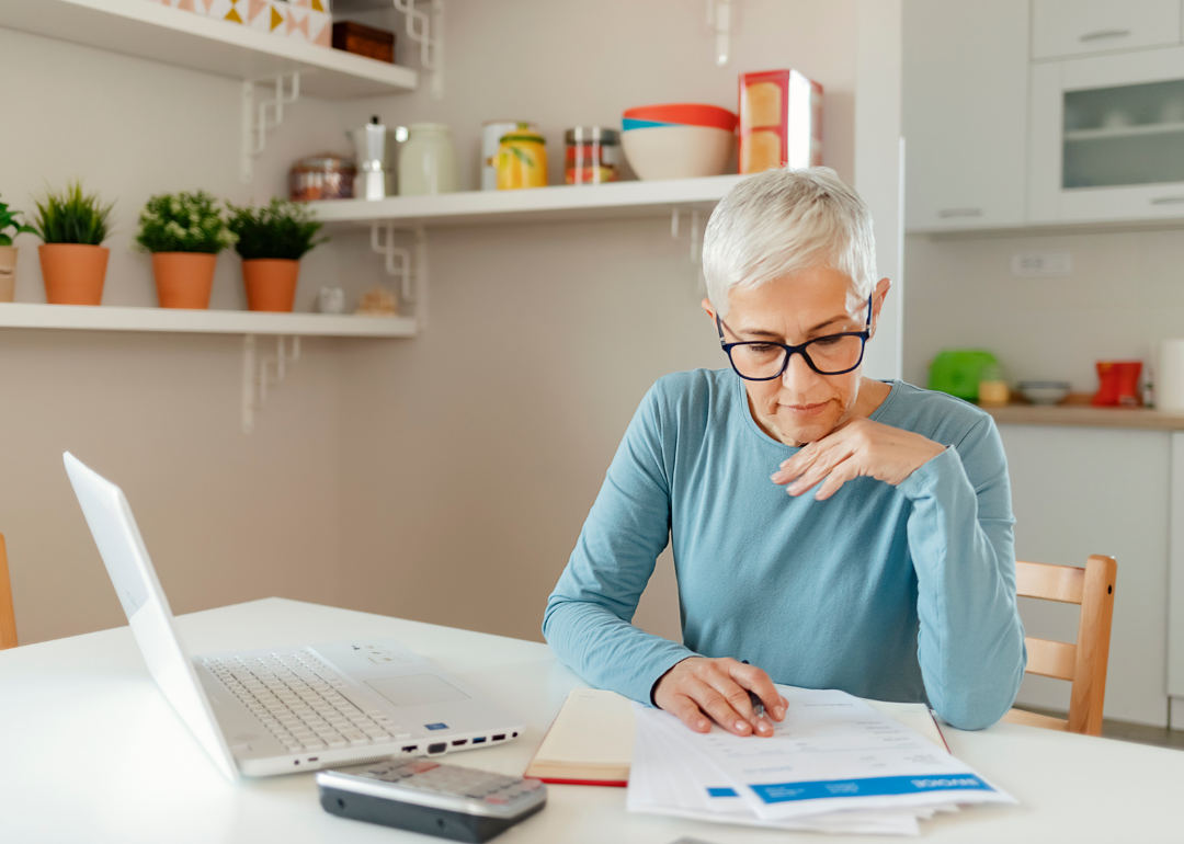 Older woman looking at documents and computer.