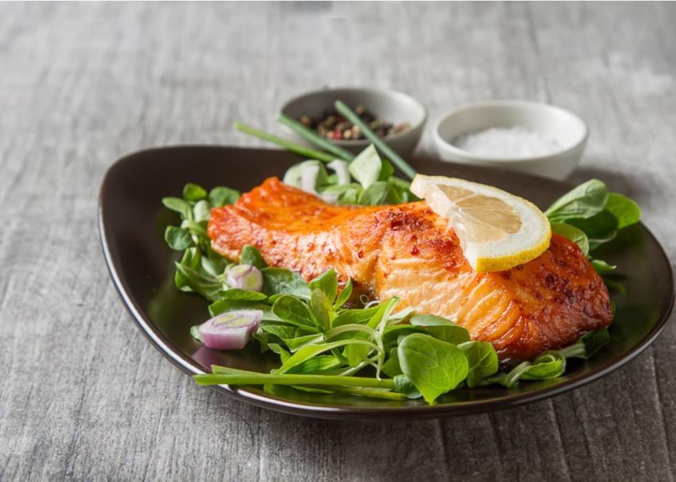 Salmon over salad with lemon on top.