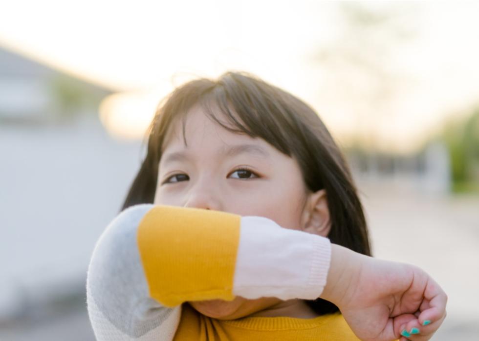 Young girl sneezing into her elbow outside.