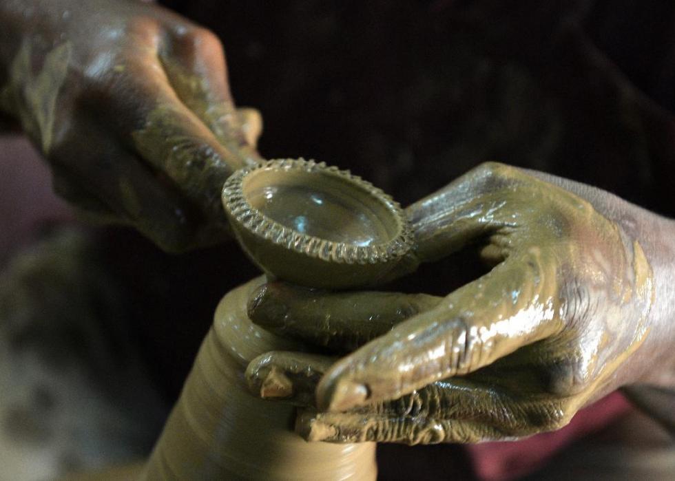 Two hands making a small clay dish on a pottery wheel. 