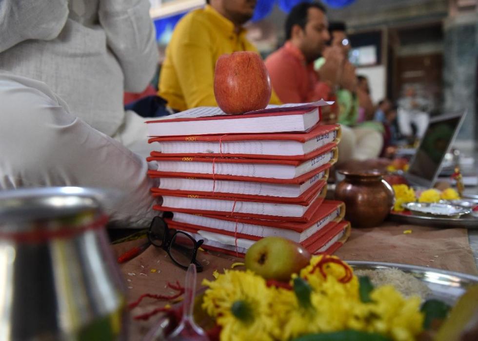 Several people sitting on the ground cross-legged in front of various objects, including books, a computer, apples, and flowers. 