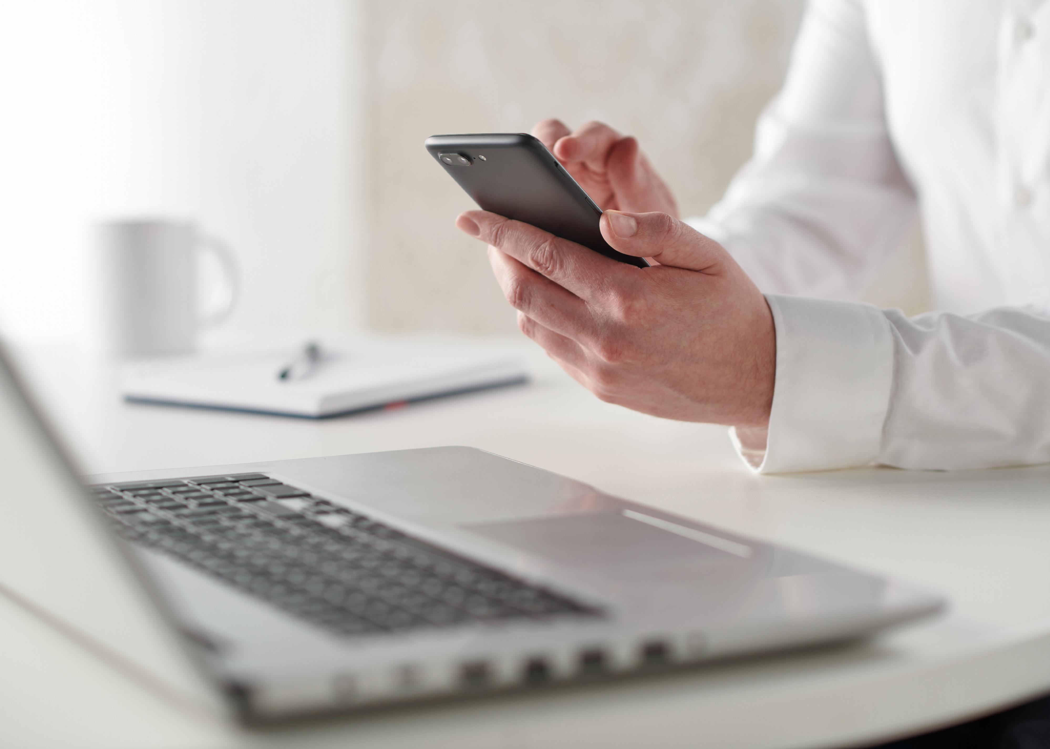 Close up of a man working at a desk with a smartphone
