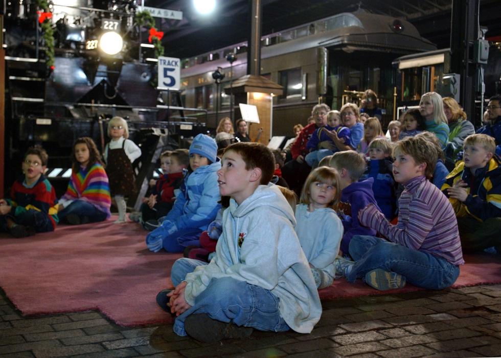 Children listen to a story at a train station.