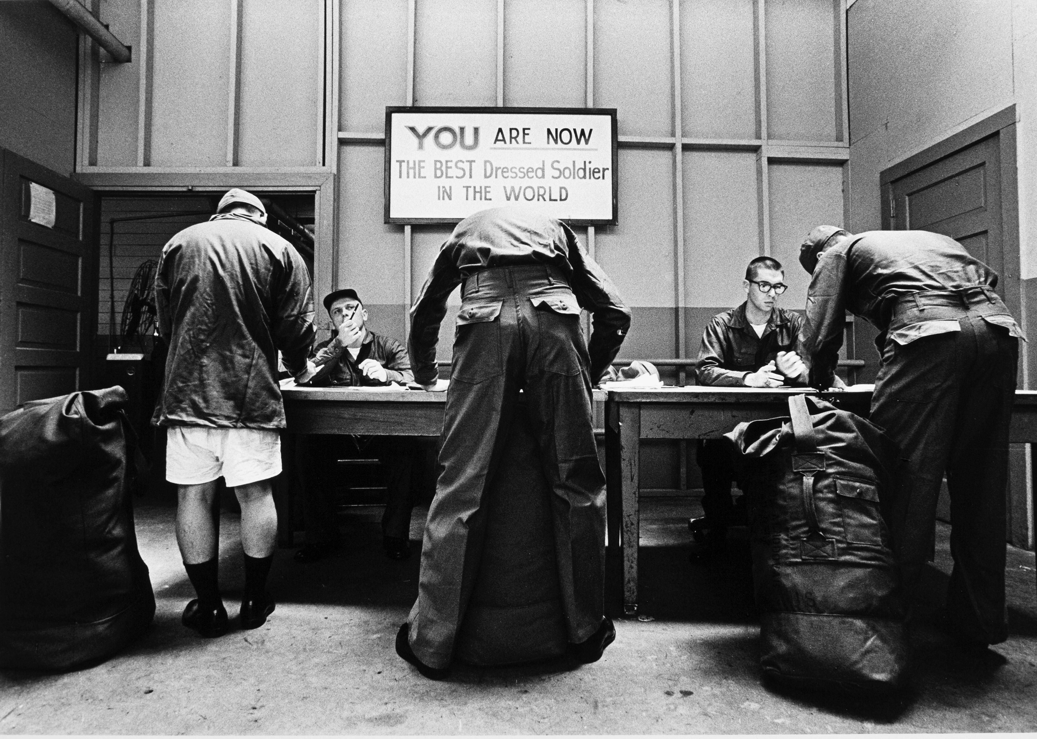 Three recently drafted soldiers sign papers under a sign that reads 'You are the Best Dressed Solider in the World' at Fort Jackson.