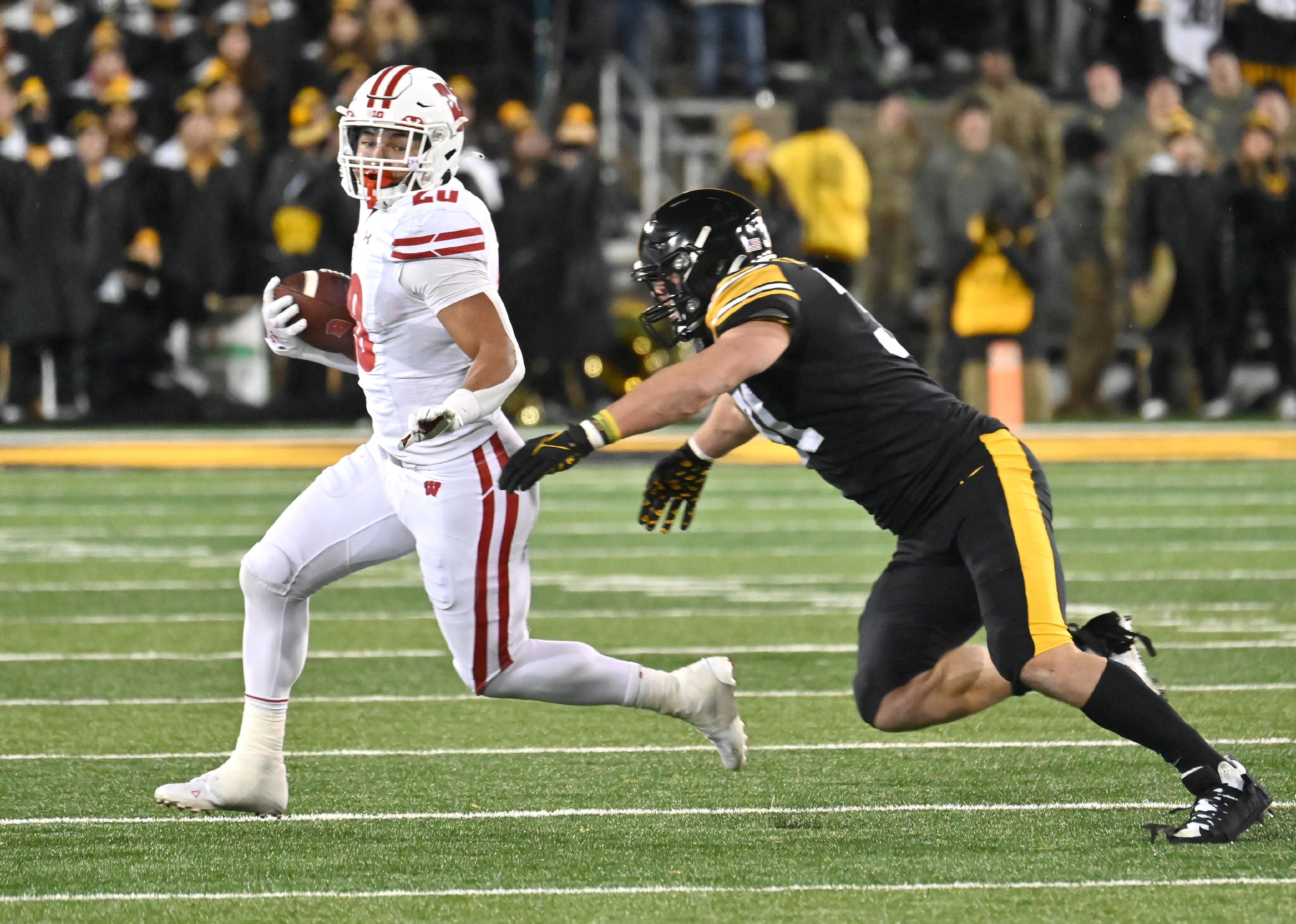 Wisconsin running back Isaac Guerendo runs after a pass reception as Iowa linebacker Jack Campbell defends.