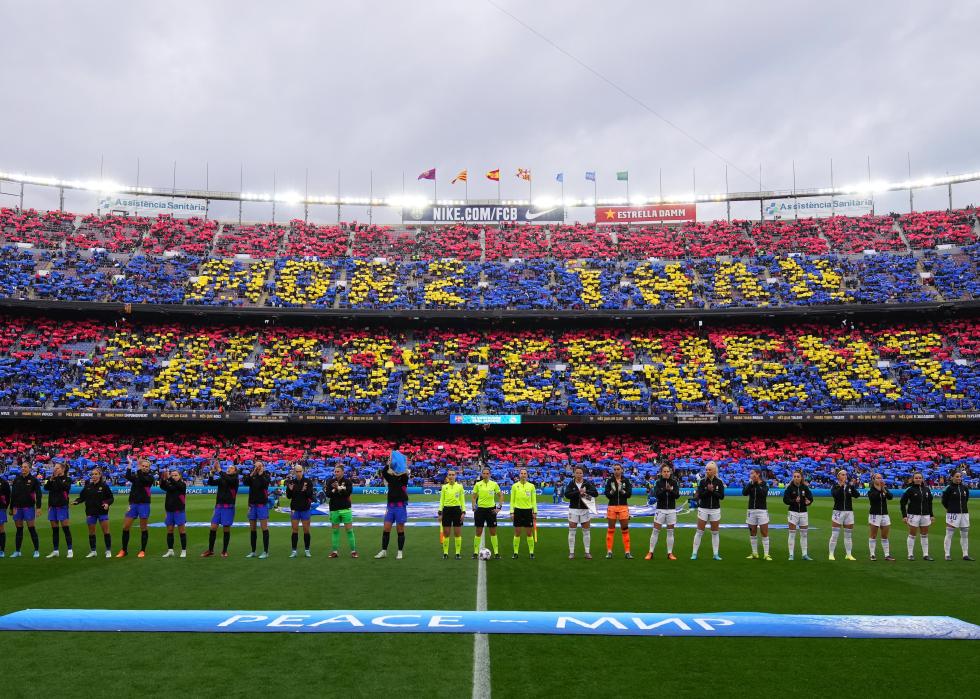 Players of FC Barcelona and Real Madrid line up as fans perform a tifo in the stands 