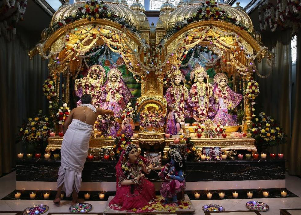 A women in a white dress approaches a highly adorned shrine inside of a temple. 