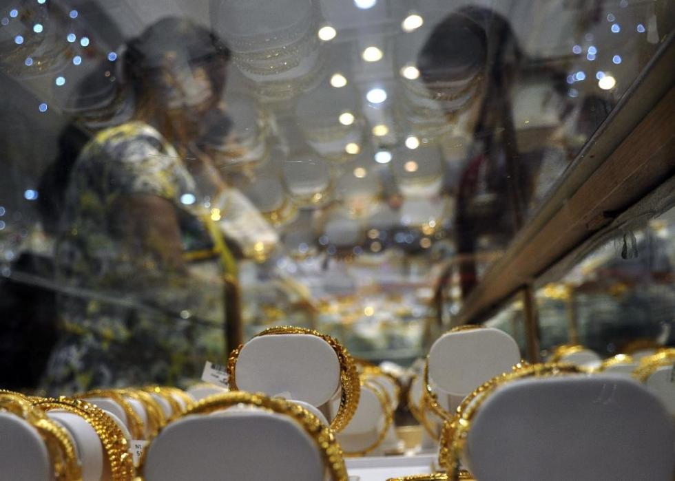 Two people talk over a case full of gold jewelry. 